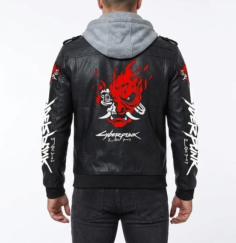 K&ouml;nnte beinhalten: Eine schwarze Kunstlederjacke mit grauem Kapuzeneinsatz. Auf der R&uuml;ckseite befindet sich eine gro&szlig;e rote Grafik einer stilisierten Oni-Maske mit Flammen und dem wei&szlig;en Schriftzug Cyberpunk 2077. Der Schriftzug Cyberpunk 2077 ist vertikal auf den &Auml;rmeln.