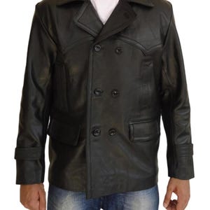 Op de afbeelding: Zwarte leren jas met een dubbele rij knopen. De jas heeft een reverskraag, twee voorzakken en knoopsluitingen. De mouwen hebben manchetten met knopen. De jas wordt gedragen over een wit shirt en een blauwe jeans.