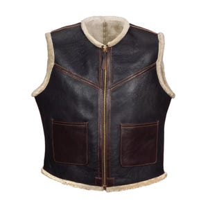 May include: A black leather vest with a shearling lining and trim. The vest features a brown leather trim, two front pockets, and a full-length gold zipper. The vest is sleeveless and has a classic, rugged design.