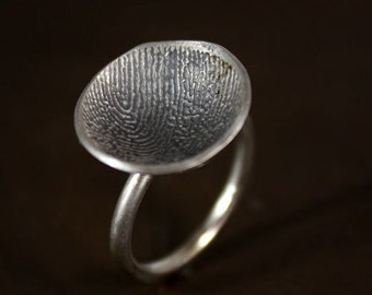 May include: A silver ring with a unique, textured, circular design. The ring is made of metal and has a smooth, polished finish.