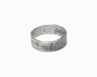 May include: A silver band ring with a fingerprint design and the word "loved" engraved on the side.