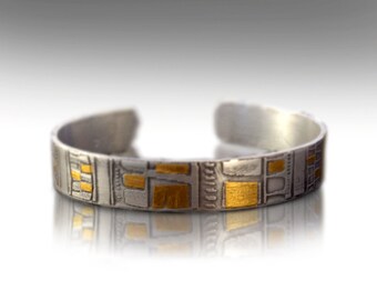May include: A silver bracelet with a geometric pattern in gold. The bracelet is made of metal and has a polished finish.