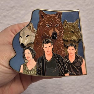 May include: A rectangular enamel pin with a gold border featuring a blue background and images of wolves and people. The pin has a brown wolf in the center, with other wolves and people around it.