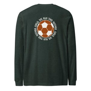 Könnte beinhalten: Dunkelgrünes Langarmshirt mit einem Fußball-Motiv. Der Fußball ist braun und weiß, umgeben von dem Text "MOTHER. GIRLS. WE RUN THIS". Das Shirt besteht aus einem weichen Material.