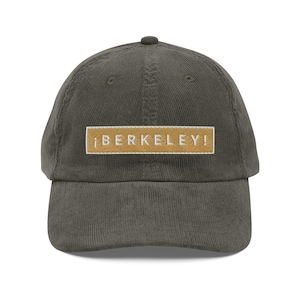 May include: A dark green corduroy baseball cap with a yellow rectangular patch that says "iBERKELEY!" in white text.
