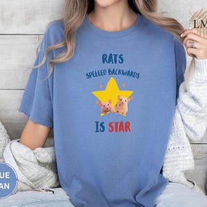 May include: Blue jean-colored t-shirt with the text "RATS SPELLED BACKWARDS IS STAR" above a yellow star graphic with two cartoon rats. The shirt is a comfortable, casual style.