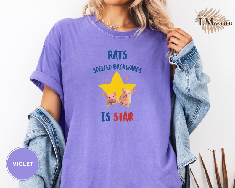 May include: Violet-colored t-shirt with the text "RATS SPELLED BACKWARDS IS STAR" in blue and red. A yellow star graphic with two cartoon rats is centered on the shirt. The shirt has rolled-up sleeves.