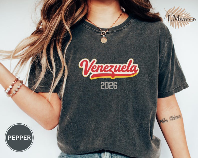 Pu&ograve; includere: T-shirt grigio scuro con la scritta "Venezuela" in rosso con contorno giallo e l'anno "2026". La maglietta &egrave; di stile casual.