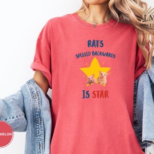 May include: A red t-shirt with the text "RATS SPELLED BACKWARDS IS STAR" in blue and red. The shirt features a yellow star graphic with two small rat illustrations. The shirt is a solid red color.