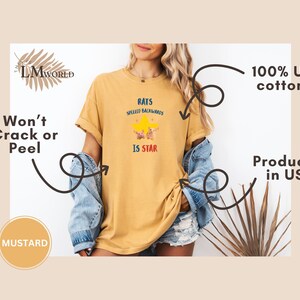 May include: Mustard-colored t-shirt with the text "RATS SPELLED BACKWARDS IS STAR" in a playful font, featuring a star graphic. The shirt is made of 100% US cotton and produced in the USA. The design is printed with a won't crack or peel guarantee.