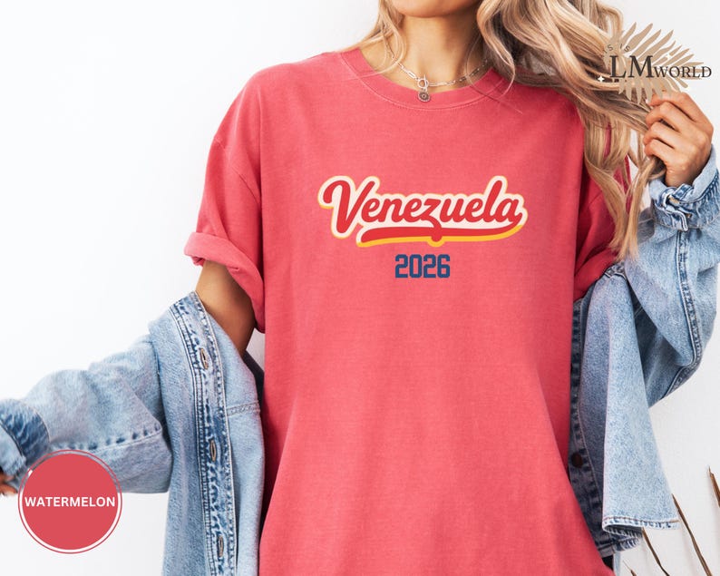Pu&ograve; includere: Una maglietta rossa con la scritta "Venezuela" in corsivo con contorno giallo e riempimento rosso. Sotto la parola "Venezuela" c'&egrave; il numero "2026" in blu. La maglietta &egrave; indossata con una giacca di jeans.
