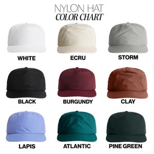 May include: A color chart for nylon hats featuring nine caps in white, ecru, storm, black, burgundy, clay, lapis, atlantic, and pine green. The text at the top reads NYLON HAT COLOR CHART, with each color name printed below its respective cap.