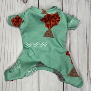 May include: A light mint green pet jumpsuit featuring a geometric pattern of brown and gray triangles and white zigzag lines. The garment has short sleeves, a crew neckline, and leg openings, designed with a soft fabric and a repeating print.