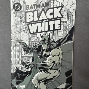 May include: Batman: Black and White comic book cover. The cover features a black and white illustration of Batman in action, set against a cityscape background. The title "Batman Black and White" is prominently displayed.