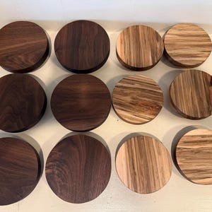 May include: A collection of twelve circular wooden discs arranged in a grid. Six discs are made of dark brown walnut wood with a smooth grain, while the other six feature a lighter, variegated wood with prominent tan and brown striped patterns.