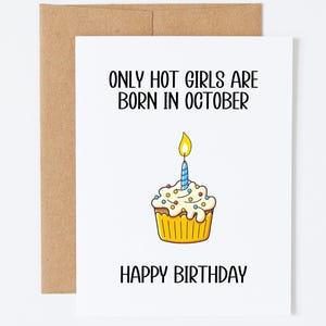 May include: A white greeting card with a brown envelope featuring the black text ONLY HOT GIRLS ARE BORN IN OCTOBER and HAPPY BIRTHDAY. In the center is a yellow cupcake with white frosting, colorful sprinkles, and a single blue lit candle.
