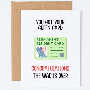 May include: A white greeting card with a brown envelope featuring the text YOU GOT YOUR GREEN CARD in black, a graphic of a light green permanent resident card with the Statue of Liberty and a flag, and the red and black text CONGRATULATIONS THE WAR IS OVER.