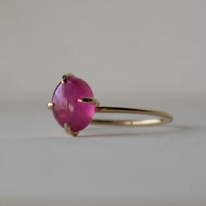 以下が含まれることがあります： 爪留めでセットされたピンクのcabochon宝石が付いた金の指輪