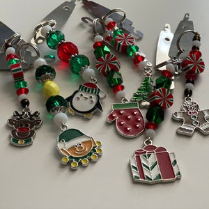 May include: A set of seven Christmas-themed keychains with various charms, including a penguin, a snowman, a mitten, a gingerbread man, a Christmas tree, a candy cane, and a gift box. The charms are attached to silver chains with red and green beads.
