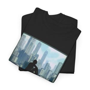 Könnte beinhalten: Schwarzes T-Shirt mit einer Grafik einer Person, die vor einer Stadtlandschaft mit hohen Gebäuden silhouettiert ist. Das Bild hat eine blaue und weiße Farbpalette, mit der Person im Vordergrund. Das T-Shirt ist gefaltet.