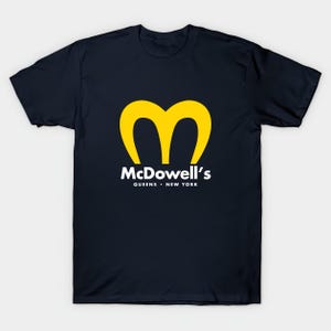 May include: Navy blue t-shirt featuring a yellow stylized "M" logo and the text "McDowell's Queens New York" in white. The shirt is a classic crew neck style, perfect for casual wear.