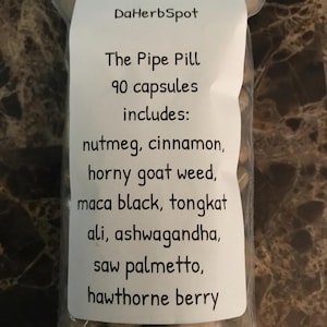May include: A clear plastic resealable bag containing 90 brown capsules. The white label reads: DaHerbSpot, The Pipe Pill, 90 capsules includes: nutmeg, cinnamon, horny goat weed, maca black, tongkat ali, ashwagandha, saw palmetto, hawthorne berry.