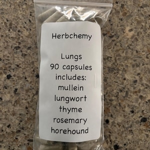 Può includere: Un sacchetto di plastica trasparente contenente capsule. Un'etichetta bianca sulla busta recita "Herbchemy" e "Lungs 90 capsules includes: mullein, lungwort, thyme, rosemary, horehound."