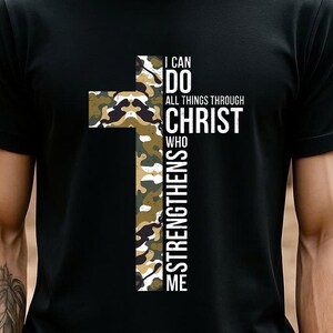 May include: Black t-shirt featuring a camouflage cross design with the text "I CAN DO ALL THINGS THROUGH CHRIST WHO STRENGTHENS ME" in white. The cross is filled with a pattern of green, brown, and tan camouflage.