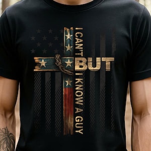 May include: Black t-shirt featuring a cross design with the text "I CAN'T BUT I KNOW A GUY." The cross incorporates elements of the American flag and a rope detail, with a rustic, weathered appearance. The design is centered on the front of the shirt.