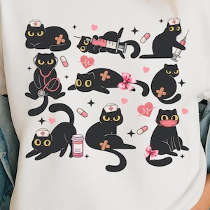 May include: White t-shirt with a black and white illustration of multiple black cats wearing nurse hats and holding medical supplies. The cats are surrounded by hearts, stars, and pills.