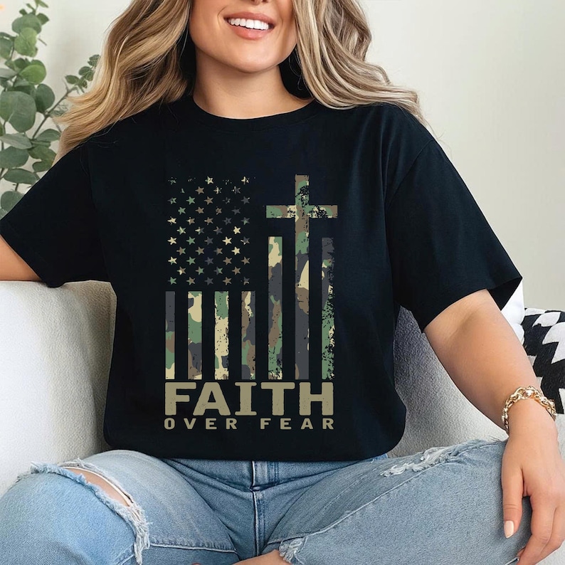 May include: Black t-shirt featuring a camouflage American flag design with a cross and the words "FAITH OVER FEAR" in a bold font. The shirt has short sleeves and a relaxed fit, suitable for casual wear.