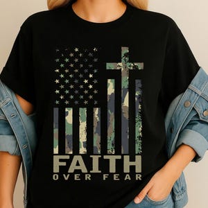May include: Black t-shirt featuring a camouflage American flag design with a cross and the text "FAITH OVER FEAR" in a distressed font. The flag incorporates stars and stripes in shades of green, blue, and brown.