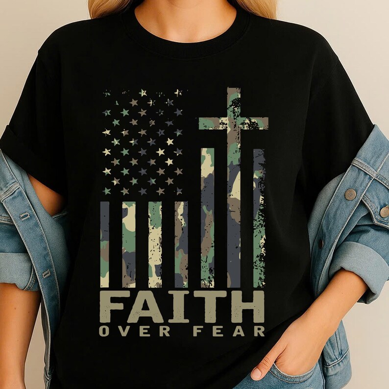 May include: Black t-shirt featuring a camouflage American flag design with a cross and the text "FAITH OVER FEAR" in a distressed font. The flag incorporates stars and stripes in shades of green, blue, and brown.