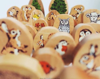 May include: Wooden animal figurines with painted details, including a rabbit, owl, fox, deer, and a lamb. The figurines are arranged on a wooden surface.