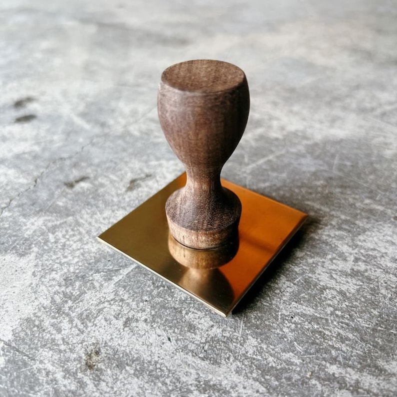 May include: A wooden stamp with a rounded top and a square brass base.