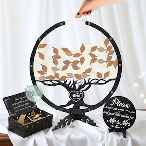 Könnte beinhalten: Alternative zum Hochzeitsgästebuch aus schwarzem Holz mit Baumdesign, blattförmigen Gästeblättern und einer Box. Der Baum hat ein Herz mit den Namen "Webb" und dem Hochzeitsdatum. Ein Schild sagt: "Bitte hinterlassen Sie Ihren Namen und Ihre besten Wünsche für Mr & Mrs."