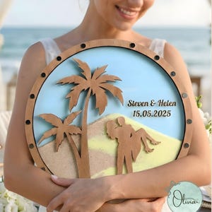 May include: Circular wooden wedding sign with a beach theme. It features a blue sky, sand, and palm trees. The sign includes the names "Steven & Helen" and the date "15.05.2025". The frame is wooden with black accents.