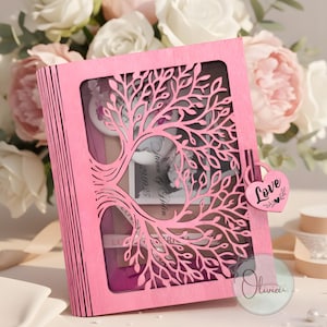 Puede incluir: Una caja rosa de madera con forma de libro con un diseño de árbol cortado en la tapa. La caja tiene un candado en forma de corazón que dice "Love". En el interior hay una foto y una tarjeta con los nombres "Liam & Helen" y la fecha "20.09.25".