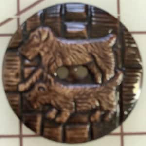 May include: A brown button with two dogs in relief. The dogs are facing the same direction and are walking. The button has a two-hole design.