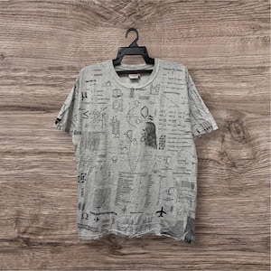 Op de afbeelding: Een grijs T-shirt met een ronde hals, bedekt met zwarte wetenschappelijke diagrammen, vergelijkingen en tekst. Het shirt toont een verscheidenheid aan symbolen en illustraties gerelateerd aan natuurkunde en wiskunde. Het woord "THERMODYNAMICS" is zichtbaar aan de onderkant.