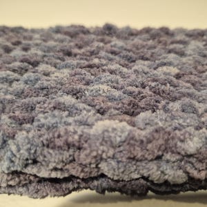 May include: Close-up of a soft, textured blanket in shades of blue and purple. The plush material has a thick, looped design, creating a cozy and inviting appearance. The blanket's color gradient adds depth and visual interest, perfect for home decor.