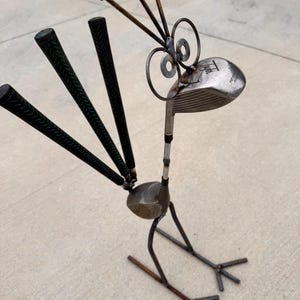 May include: A whimsical metal sculpture of a bird, crafted from repurposed golf clubs and nails. The bird features a golf club head as its head, golf club grips as feathers, and nails as the crest. The sculpture is a unique piece of art.