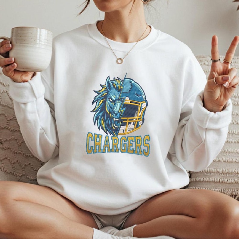 Puede incluir: Una sudadera blanca de manga larga con un gr&aacute;fico de una cabeza de caballo dividida con un casco de f&uacute;tbol americano en azul y amarillo. Debajo del gr&aacute;fico, la palabra CHARGERS est&aacute; impresa en letras amarillas con un borde azul.