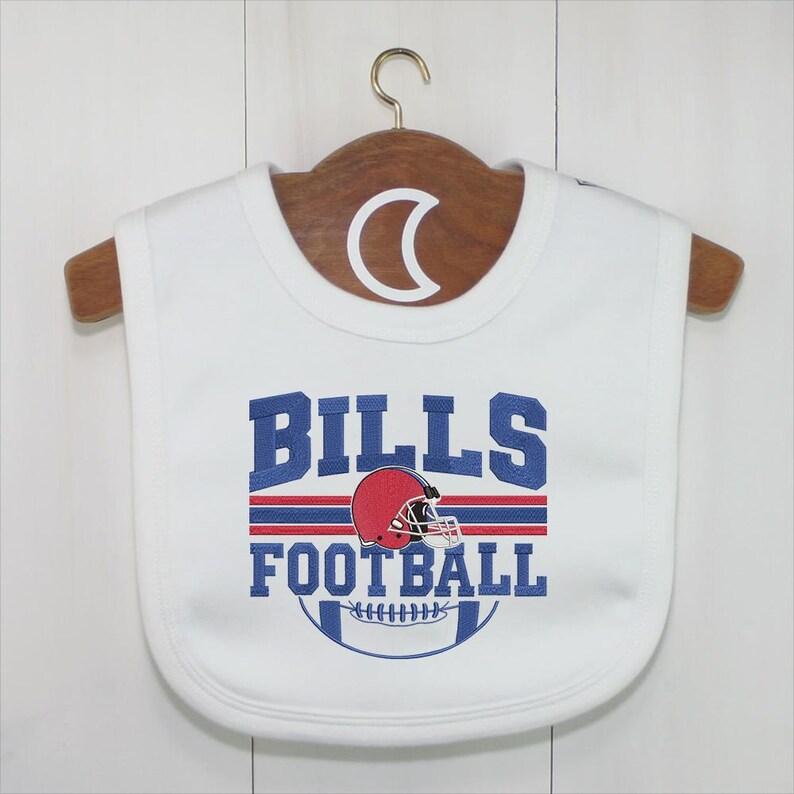May include: White baby bib with the text "BILLS FOOTBALL" in blue, red, and white. The design includes a red football helmet and a football graphic. The bib is hanging on a wooden hanger.