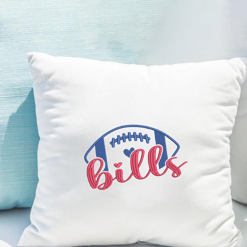 May include: White square pillow with a blue and red embroidered football design. The design includes a football shape with vertical stripes and the word "Bills" in a cursive font.