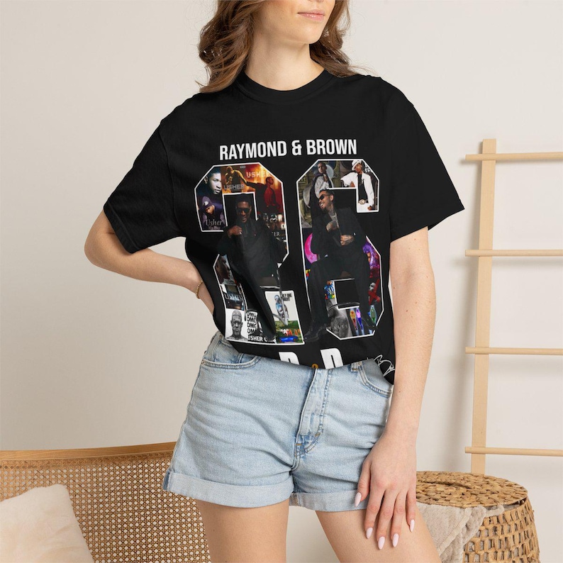 Pu&ograve; includere: T-shirt nero con la scritta "RAYMOND & BROWN" sopra il numero "26". Il numero &egrave; riempito con un collage di immagini. La modella indossa pantaloncini di jeans azzurri.