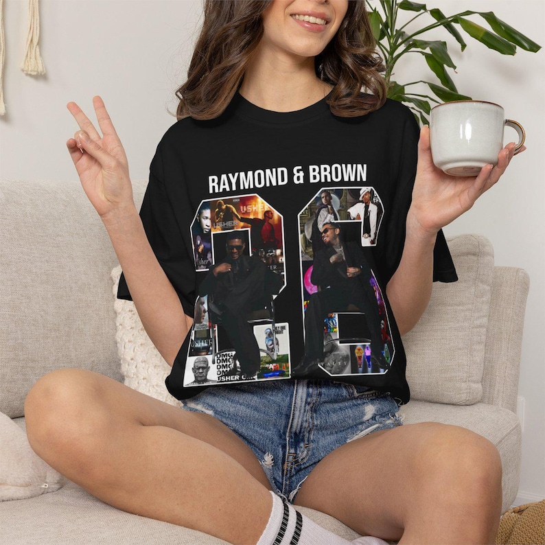 Pu&ograve; includere: T-shirt nero con la scritta "RAYMOND & BROWN" sopra una grande grafica "26". La grafica &egrave; riempita di immagini di un musicista. La persona nella foto indossa pantaloncini di jeans e tiene in mano una tazza.