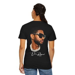 Pu&ograve; includere: T-shirt nero con un ritratto di Usher con occhiali da sole e collana a catena. L'immagine include il testo "Usher Raymond" in corsivo. La maglietta &egrave; un classico girocollo.
