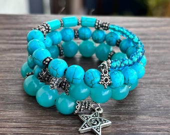 May include: Three-strand bracelet set featuring turquoise beads and silver-toned accents. The bracelets have a mix of round and cylindrical beads, with a star-shaped charm dangling from one. The jewelry is displayed on a wooden surface.