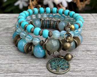 May include: A set of three bracelets with turquoise, blue, and clear beads. The bracelets have large blue-grey beads, bronze-coloured accents, and a tree charm. The word "BlooMoon" is visible in the bottom right corner.